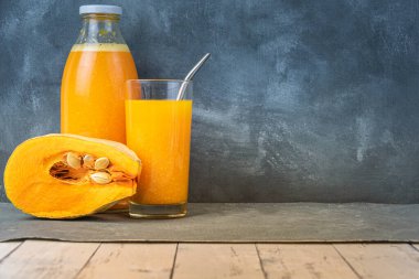 Bardakta taze sıkılmış kabak suyu. Şişe, arka plandaki ahşap masada sarı meyve suyuyla dolu. Bir parça hamurlu balkabağı. Vejetaryen kahvaltısı, sağlıklı yemek.