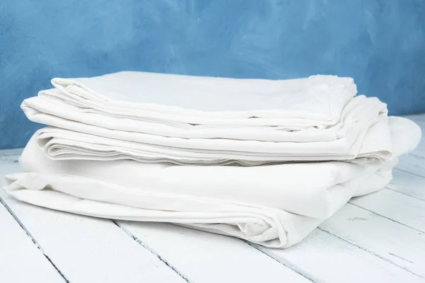 Stack of white sheets on wooden table. Folded fabric. Clean and ironed tablecloths. Bed linen is washed and prepared for guest