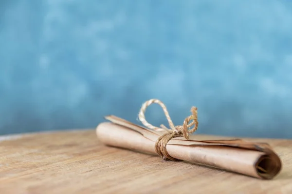 Roll of vintage parchment tied with rope on wooden. Blue wall as background