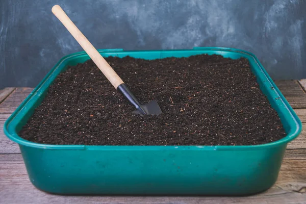 Preparation of garden soil for seedlings. Peat is in green container on table. Home spring gardening . Small shovel for working in ground