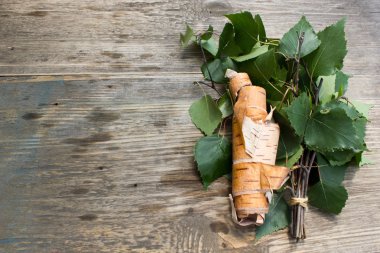 Green leaves and birch bark on a wooden background, space for text