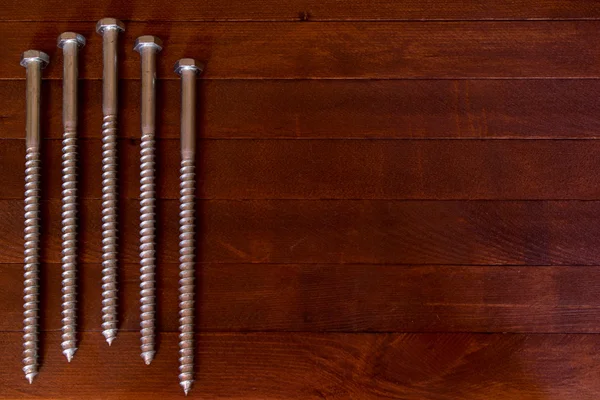 Dlouhé kovové šrouby na dřevěný stůl — Stock fotografie
