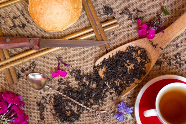 Schuss aus dem trockenen schwarzen Tee mit Blumen, eine Tasse auf Pralinenhintergrund — Stockfoto