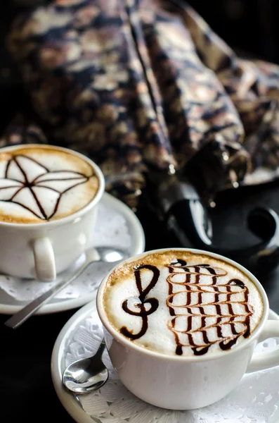 yanlarında bir masada köpük stand bir desenle cappuccino kahve ile bir şemsiye, bu.