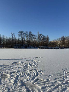 Buz ve karla kaplı bir nehrin manzarası. Kışın ve mavi gökyüzünde insanların ayak izleri var.