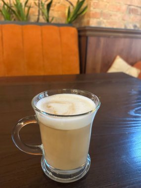 Ahşap masada kalp şeklinde köpüklü cam bir fincan latte.