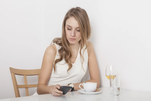 Блондинка шевелит кофе, глядя на мобильный телефон. — стоковое фото