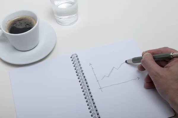 Hand schetsen in een notitieblok met een kopje koffie en een glas water — Stockfoto