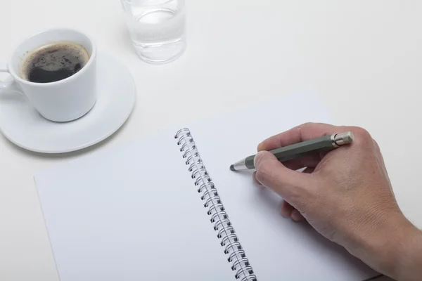 Someone writes down a note to his hotebook lying on the desktop Stock Photo