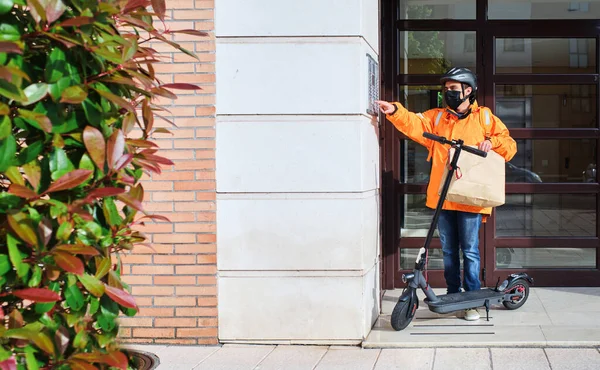 delivery man with face mask and electric scooter rings doorbell to deliver a package