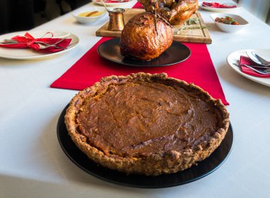 Balkabağı turtası, füme jambon, fırında hindi, et suyu, patates püresi, jöleli havuç, çatal bıçak seti beyaz masa örtüsü ve kırmızı masa koşucusu.
