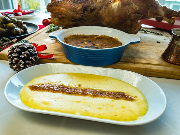 Kızarmış hindi, et suyu ve mısır ekmeği. Tahta kesme tahtasına patates püresi, brussel filizi, çatal bıçak seti, beyaz masa örtüsü ve kırmızı masa koşucusuyla süslenmiş.