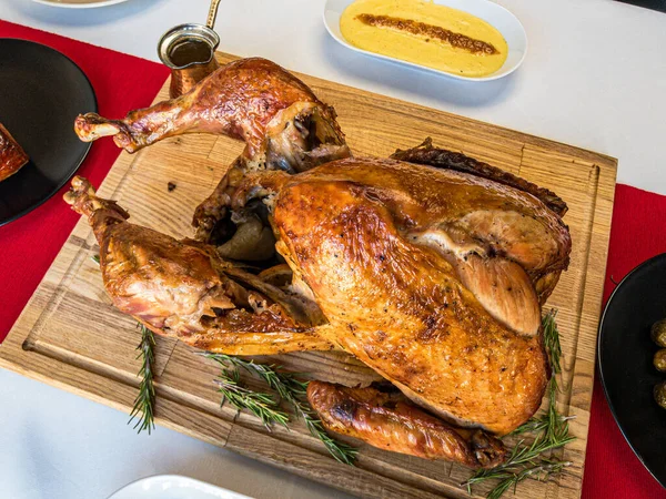 Tam pişmiş hindi, biberiye filizi ve ahşap bir kesme tahtasına sos, arkasında patates püresi, beyaz masa örtüsü ve kırmızı masa koşucusu.