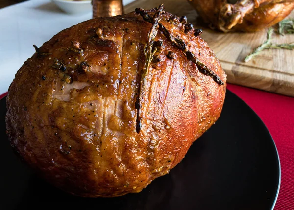 Glazed smoked ham with rosemary and clove, and whole roast turkey, gravy, mashed potatoes and tableware on the background on a white tablecloth and red table runner, top side vew, close up