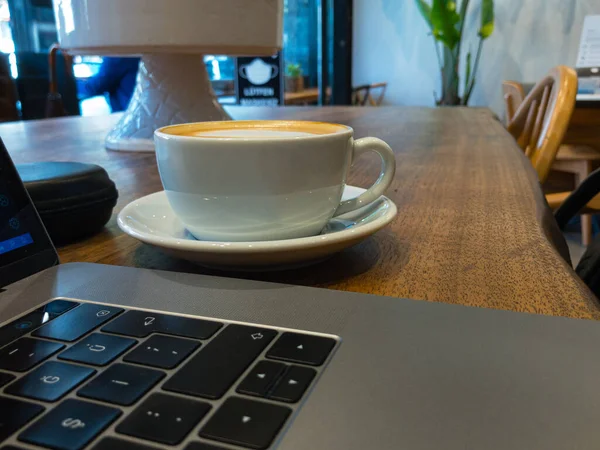 Yazılım geliştiricisi olarak tahta masada dizüstü bilgisayarla çalışırken kafeteryada kahve içmek.