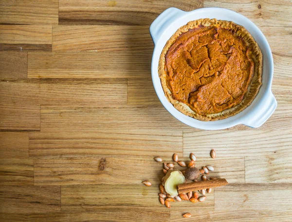 Balkabağı baharatlı ev yapımı tereyağlı turta, tarçın çubuğu, zencefilli hindistan cevizi ve tahta yüzeyde fotokopi alanı olan birkaç kabak tohumu.