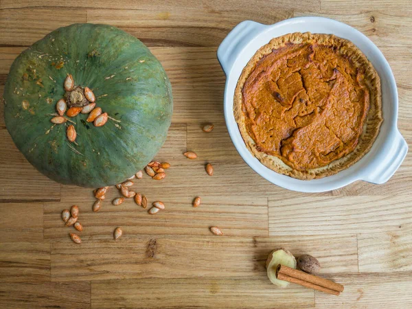 Kabak ezmeli ev yapımı tereyağlı kabak turtası, tarçın çubuğu, zencefilli hindistan cevizi ve ahşap bir yüzeyde birkaç kabak çekirdeği.