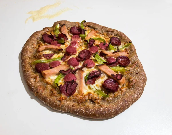 Beyaz bir yüzeyde ev yapımı tam buğday pizzası ve yüzeyinde irmik var.