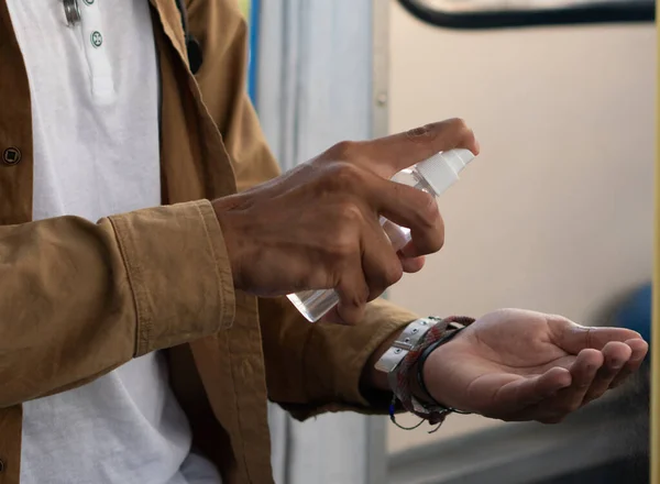 Latino man sanitizing his hands with alcohol spray to go to college