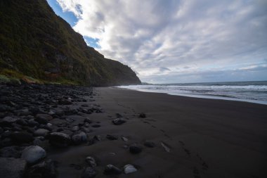 Yeşil bitki örtüsü ve kumların üzerinde yürüyen bir insanın basamakları olan kayalıklarda parlayan volkanik kumsal.