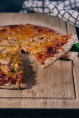 Tavuk ve pastırma parçalarıyla hazırlanmış pizza, tahtanın üzerinde sunuluyor..