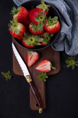 Siyah arka planda taze çilekler, bir ahşabın üzerine serilmiş..