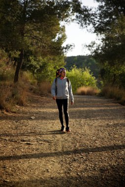 Spor elbiseli ve sırt çantalı bir kadın ağaçların arasında dağları keşfediyor..