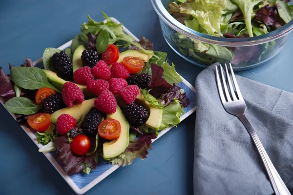 Kırmızı böğürtlenli salata, vişneli domates ve avokado, mavi bir masada..