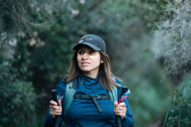 Yürüyüş direkleri olan bir kadın ağaçlarla ve çalılarla dolu bir yolda yürüyor..