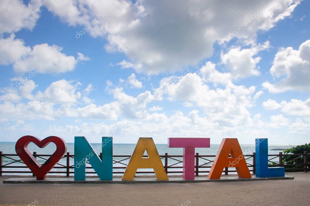 arriving signage tourism board with Natal inscription in large, colorful letters on the beach and sea in the city of Natal, state of Rio Grande do Norte, Brazil