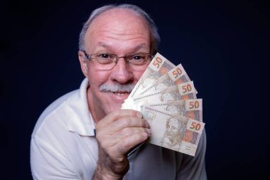 Kameraya gülümseyen ve elinde Brezilya 'nın gerçek para banknotları tutan beyaz bir adam.