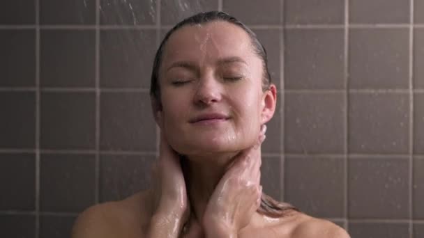 Привлекательная брюнетка средних лет принимает душ. Голая женщина моет волосы. Серый кафель на стенах. Забота о коже, рутинные домашние процедуры. — стоковое видео