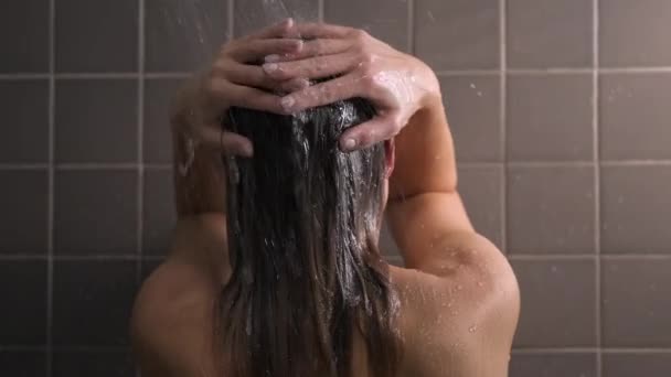 Aantrekkelijke brunette vrouw van middelbare leeftijd neemt een douche. Naakte vrouw wast haar haar. Grijze tegel op de muren. Verzorging van de huid, routine thuisbehandelingen. — Stockvideo