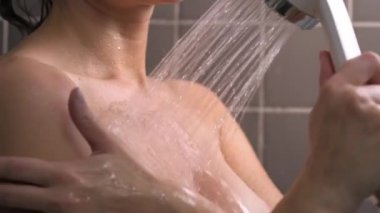 Çekici esmer, orta yaşlı kadın duş alıyor. Kadın saçını yıkıyor. Çıplak vücut. Duvarlarda gri fayans var. Cilt bakımı, rutin ev tedavileri.