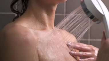 Çekici esmer, orta yaşlı kadın duş alıyor. Kadın saçını yıkıyor. Çıplak vücut. Duvarlarda gri fayans var. Cilt bakımı, rutin ev tedavileri.