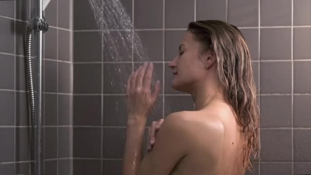 Atrakcyjna brunetka w średnim wieku bierze prysznic. Naga kobieta myje włosy. Szara płytka na ścianach. Opieka nad skórą, rutynowe zabiegi domowe. — Wideo stockowe