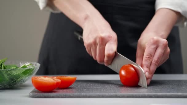Una chef con uniforme blanco y un delantal negro en la cocina del restaurante. El cocinero corta las verduras con un cuchillo de cocina grande. — Vídeos de Stock