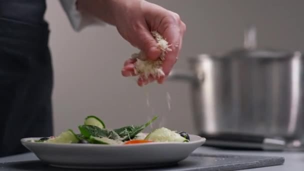 Kuchařka v bílé uniformě a černá zástěra v kuchyni restaurace. Vařím. Kuchař posype strouhaným sýrem připravené jídlo. — Stock video