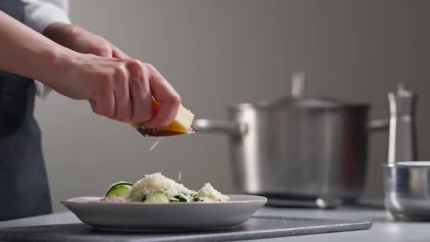 A female chef in a white uniform and a black apron in the restaurant kitchen. Cooking a salad. The cook rubs the parmesan cheese on a small grater. — Stock Video