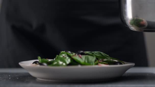 Une cuisinière en uniforme blanc et un tablier noir dans la cuisine du restaurant. Le cuisinier verse de la sauce à salade de canneberges rouges. Fabrication et décoration des aliments. — Video