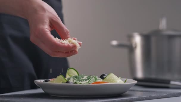 En kvinnlig kock i vit uniform och ett svart förkläde i restaurangköket. Matlagning. Kocken strör riven ost tillagad mat. — Stockvideo