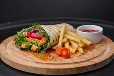 İnce hamurlu tortilla ve sebze ve salatayla pişirilmiş tavuk dürümü. Tahta kesme tahtasında patates kızartması ve sos ile servis edilir..