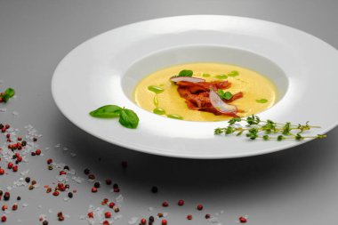 Fesleğenle süslenmiş füme etli mısır kremalı çorba, gri bir arka planda. Restoran menüsündeki ilk yemek..