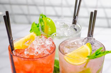Üç ferahlatıcı yaz kokteyli bardakta ve bar rafında tüpler..