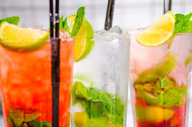 Üç ferahlatıcı yaz kokteyli bardakta ve bar rafında tüpler..