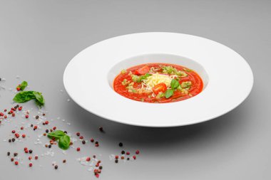 Beyaz tabakta gri bir arka planda peynirli domates çorbası çorbası..