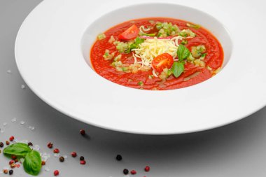 Beyaz tabakta gri bir arka planda peynirli domates çorbası çorbası..