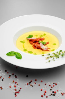 Fesleğenle süslenmiş füme etli mısır kremalı çorba, gri bir arka planda. Restoran menüsündeki ilk yemek..