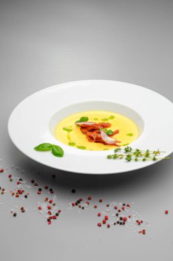 Fesleğenle süslenmiş füme etli mısır kremalı çorba, gri bir arka planda. Restoran menüsündeki ilk yemek..