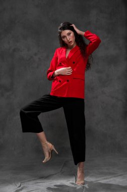 Siyah arka planda, kırmızı ceketli, uzun siyah saçlı, güzel, doğulu bir kadın. Model stüdyoda poz veriyor..